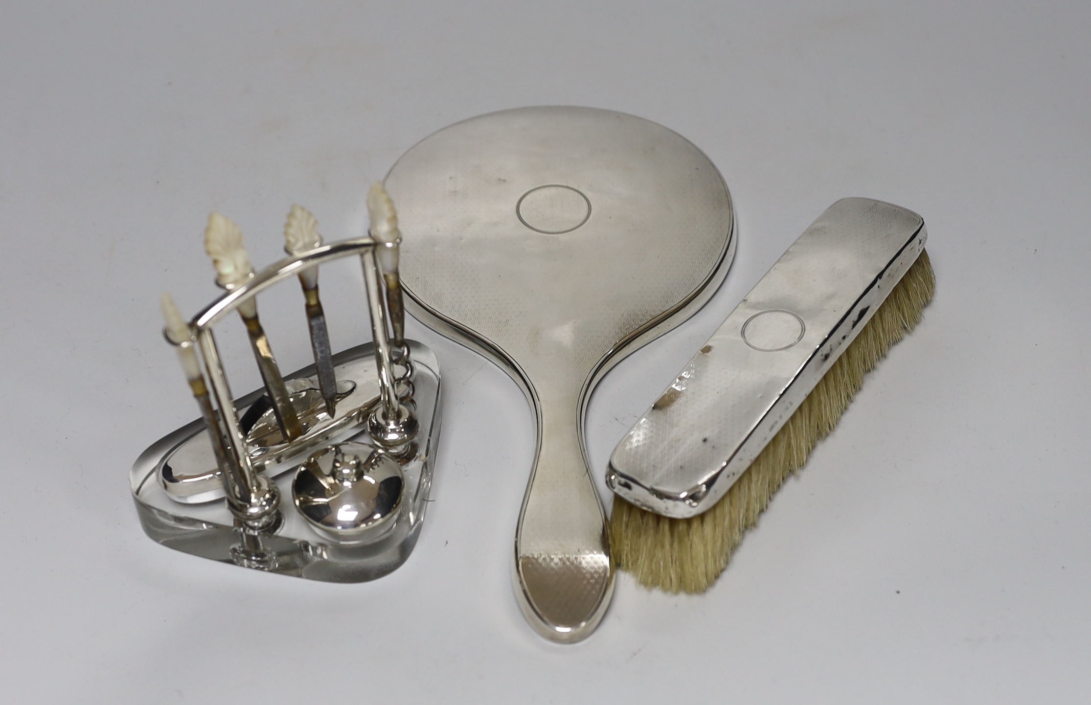 A George V silver mounted glass manicure stand with six accessories, height 12.5cm, a similar silver mounted hand mirror and brush.